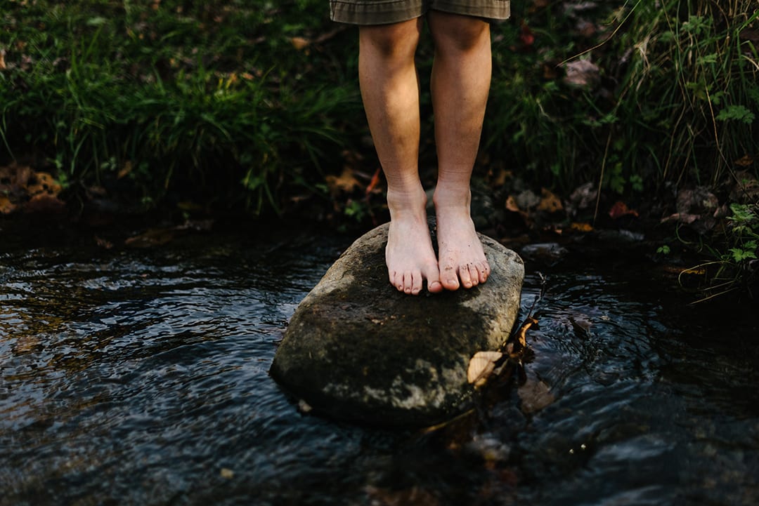 Barefoot child standing on a rock in a stream