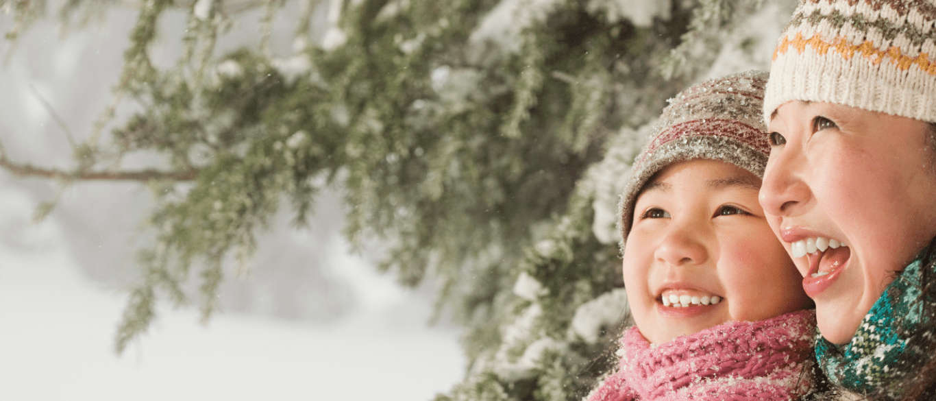 Smiling mother and daughter dressed in winter clothing outside in the snow